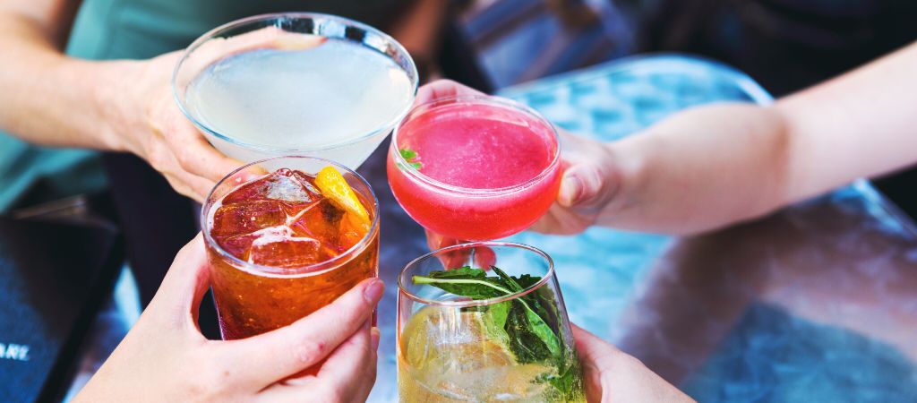 Four hands clink glasses with colorful cocktails outside. Clinking Colorful Cocktails