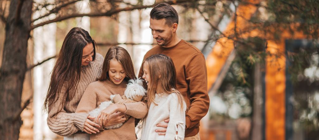 Family Holding Their Dog at a Smoky Mountain Cabin A young family with a father, mother, and two daughters smiling and holding a small dog in front of a Smoky Mountain cabin.