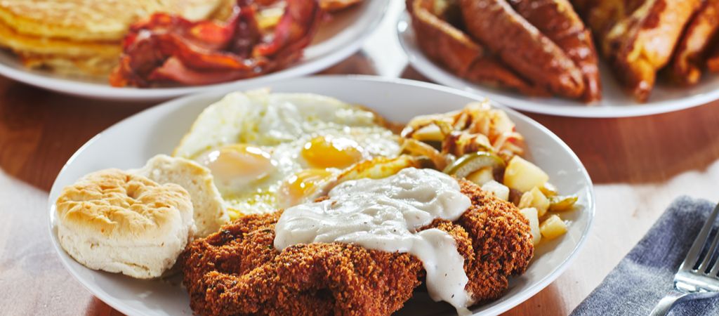 A plate loaded with eggs, hash, fried steak with gravy, and a biscuit showcases a classic Southern breakfast, with 2 additional plates in the background. Southern Breakfast Dishes