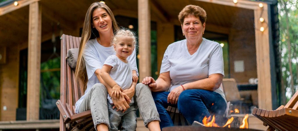 Women Generations by a Firepit at a Smoky Mountain Cabin A grandmother, mother, and young daughter sit and smile around a firepit in front of a Smoky Mountain cabin.