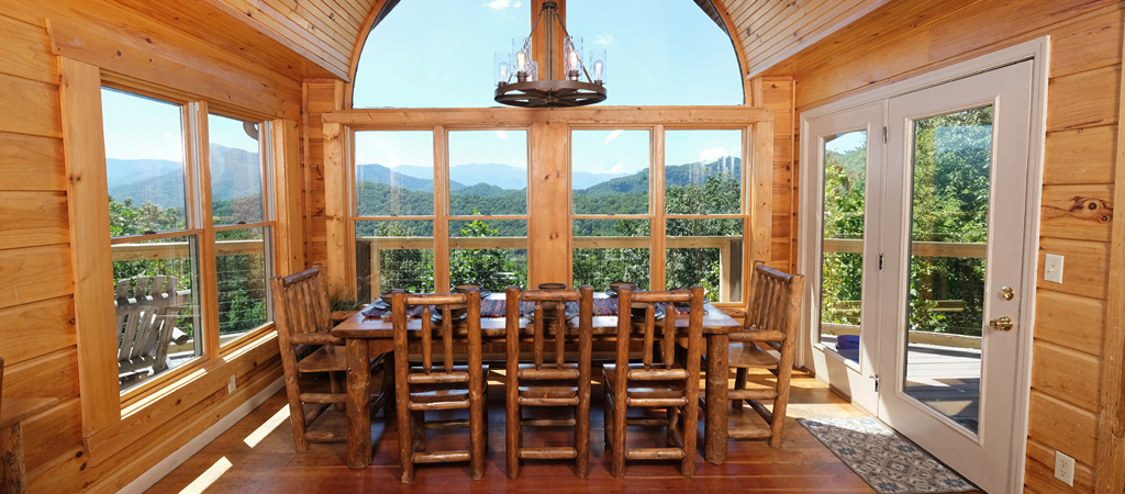 Cabin Dining Table with a Smoky Mountain View Log dining table set in front of a wall of windows framing Great Smoky Mountain views at a cabin rental.