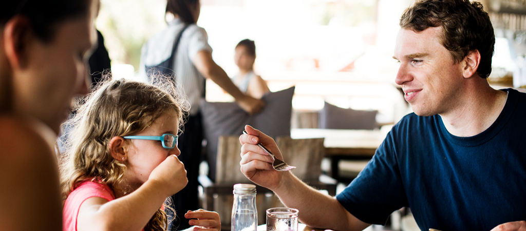 Family Having Breakfast at a Restaurant A father helps feed his young daughter with a smile at a restaurant.