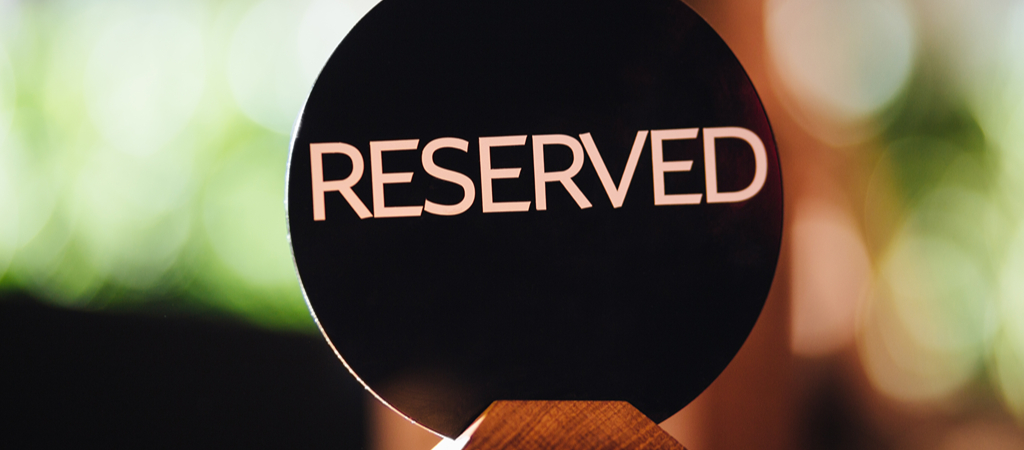 Reserved Sign on a Restaurant Table A card set on a restaurant table that reads Reserved, with blurred greenery in the background.